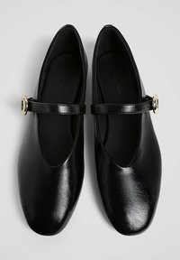 Ballerine in pelle nera con punta arrotondata, caratterizzate da una tomaia elegante, una fascia sul dorso del piede e un accento in fibbia color oro. Suola piatta.