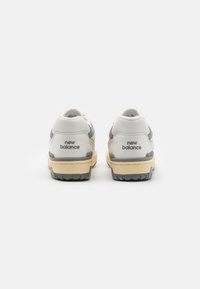 Fehér és szürke sportcipők, textúrált bőr felsőrésszel, "new balance" logóval a sarkán, és bézs talppal, melynek mintázott érintkezési felülete van.