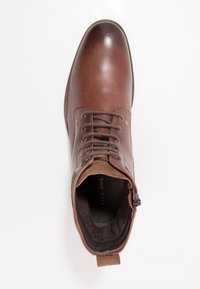 Bottine en cuir marron avec une finition lisse, un laçage frontal et un intérieur doux. Comprend une fermeture éclair latérale et un rembourrage autour de la cheville.