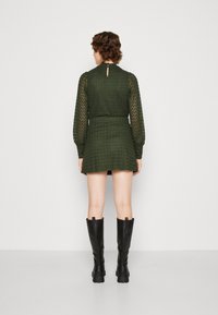 Vestido verde con patrón texturizado, mangas largas y detalle de abertura en la parte posterior. Combinado con botas de cuero negras hasta la rodilla.