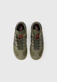 Zelená teniska s texturovaným svrškem, černými pruhy a oranžovým logem. Má kulaté tkaničky a polstrovanou stélku. Gumová podrážka pro lepší přilnavost.