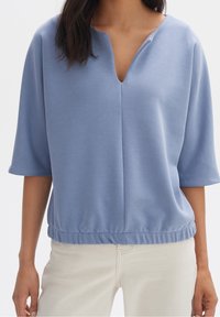Maglietta corta azzurro chiaro con scollatura a V, vestibilità comoda e orlo arricciato. Tessuto liscio con una leggera lucentezza, perfetta per un look casual.