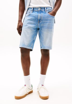 Wyblakłe, jasnoniebieskie szorty dżinsowe o prostym kroju, pięć kieszeni i przeszycia. Noszone z białymi trampkami i skarpetkami.