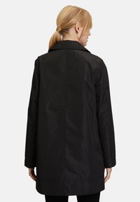 Czarny wodoodporny płaszcz o luźnym kroju, z kaszmirowym kołnierzem i długimi rękawami. Gładka tekstura i minimalistyczny design bez widocznych detali.