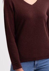 Burgunderfarbener Strickpullover mit V-Ausschnitt, langen Ärmeln und einer strukturierten Oberfläche, kombiniert mit hellblauen Jeans.