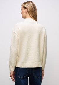 Krämfärgad stickad tröja med ribbad halsringning och muddar, med en avslappnad passform och en mjuk textur, kombinerad med mörk tvättade jeans.
