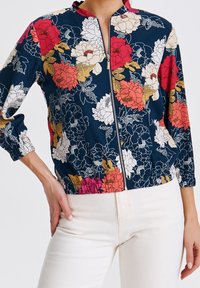 Chaqueta con cremallera y estampado floral que presenta un fondo azul marino, patrones de flores multicolores y elásticos en el dobladillo y las mangas. Tela ligera.