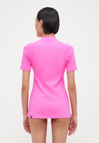 Short-sleeve, fitted rash guard in bright pink with vertical ribbed texture and a mock neck design, featuring a small logo at the hem.