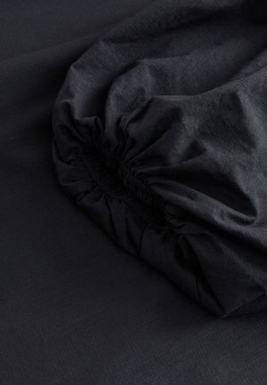 Black fabric with a smooth texture and a gathered, elasticized edge, showcasing a subtle sheen and fine weaved patterns.