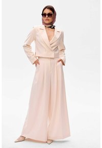 Cropped, dubbelgeknoopt blazer en wijduitlopende broek van lichtroze stof. Afgewerkt met een gebloemd hoofddoek en zonnebril.