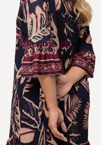Robe marine avec imprimé floral rose et bordeaux, manches évasées avec ourlet froncé et texture douce ; corsage ajusté avec coupe décontractée.