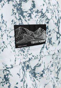Tissu marbré blanc et gris avec une patch noire montrant des lignes de contour blanches de montagnes et le texte "TECH FUSION" et "JACK & JONES".