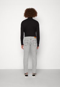 Harmaat farkut suoralla leikkauksella, takataskut yksityiskohtaisesti kirjailtu ja varustettu brändätyllä nahkapalalla. Yhdistetty mustaan poolopaitaan.