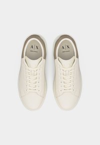 Ζευγάρι λευκά αθλητικά παπούτσια Armani Exchange χαμηλού στυλ με μπεζ λεπτομέρειες, κλείσιμο με κορδόνια και λογότυπο A|X στις εσωτερικές σόλες.