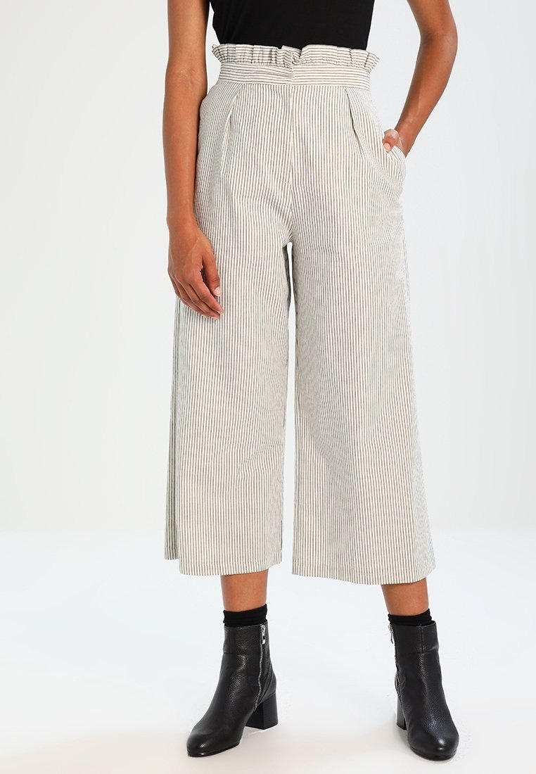 Striped wide-leg pants in white and light gray with a ruffled waistband and side pockets, paired with black ankle boots.
