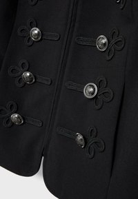 Gros plan sur un tissu noir avec des boucles tressées décoratives et des boutons gravés en argent disposés en deux rangées verticales.