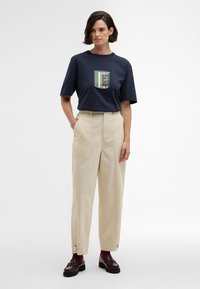 T-shirt azul-marinho com um gráfico listrado colorido ao centro, combinado com calças bege de cintura alta e textura canelada, e sapatos de camurça escuros.