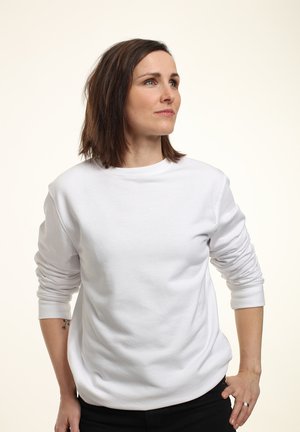 Maglione bianco a maniche lunghe con polsini a costine, colletto tondo e vestibilità comoda. Tessuto liscio, indossato con pantaloni scuri.