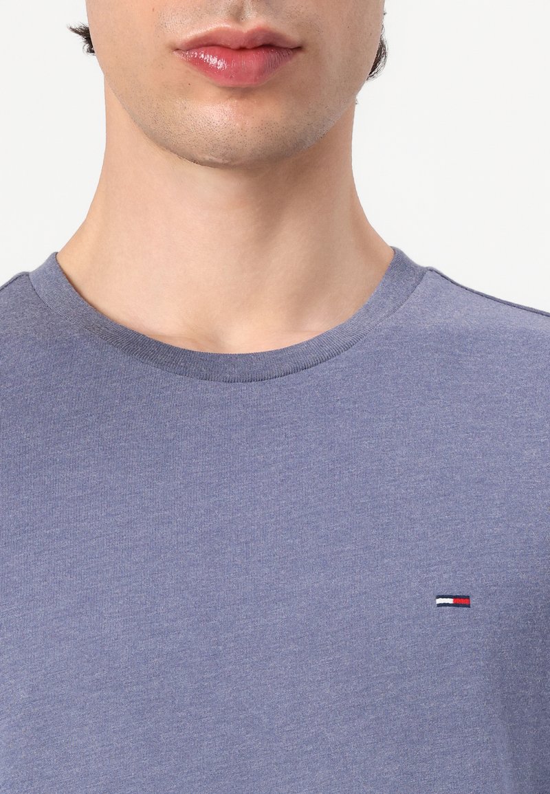 Bavlněné tričko v tlumené modré barvě s kulatým výstřihem. Má malé, barevné logo na hrudi. Měkká textura, volný střih.