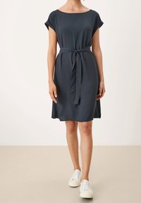 Mörkblå klänning i lätt tyg, med bälte i midjan, korta ärmar och avslappnad passform. Matchas med vita sneakers.