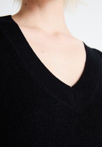 Black knitted sweater featuring a deep V-neck design, ribbed texture, and a fitted silhouette, with no additional hardware or patterns.