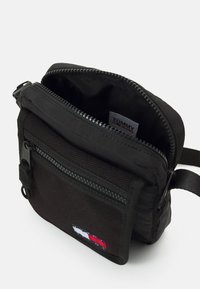 Borsa a tracolla in nylon nero con scomparto principale con zip, tasca anteriore e patch logo Tommy Jeans in rosso, bianco e blu. Superficie testurizzata.