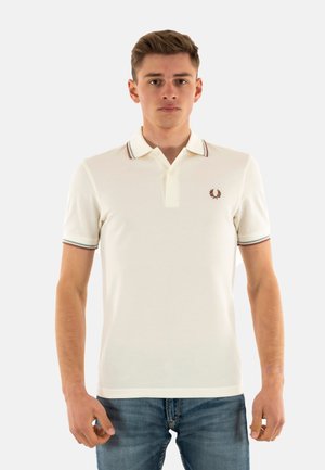Polo bianco con colletto a coste caratterizzato da strisce verdi e rosse. La maglietta presenta un piccolo emblema ricamato sul lato sinistro del petto.