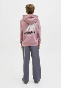 Lila huvtröja med "core dept." logotyp och grafik på baksidan, tillsammans med löst sittande grå sweatpants. Mjuk bomullsmaterialtextur.