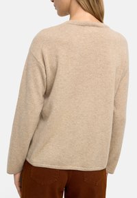 Beżowy sweter dziany z okrągłym dekoltem, opadającymi ramionami i miękką teksturą. Posiada prążkowane krawędzie oraz luźny krój z tyłu.