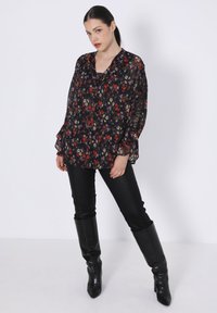 Black floral blouse with long, bell sleeves, sheer texture, and a v-neck design, paired with shiny black fitted pants and knee-high footwear.