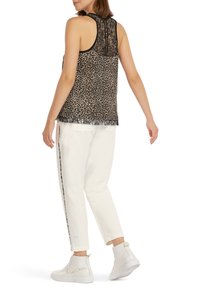 Tijgerprint tanktop met zwarte kanten achterkant, vergezeld van witte joggers en witte hoge sneakers.