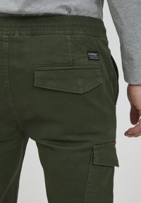 Groene cargo broeken van textuur katoen, met een elastische tailleband en een klepzak op de achterkant met een merketiket.