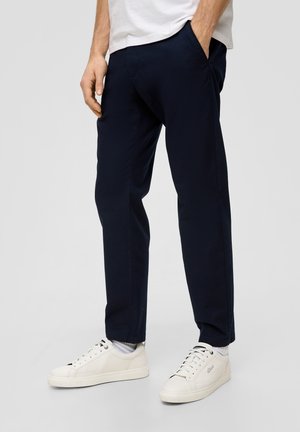Navy blue tapered pants made of textured fabric, featuring side pockets and paired with white sneakers, showcasing sleek design and clean lines.