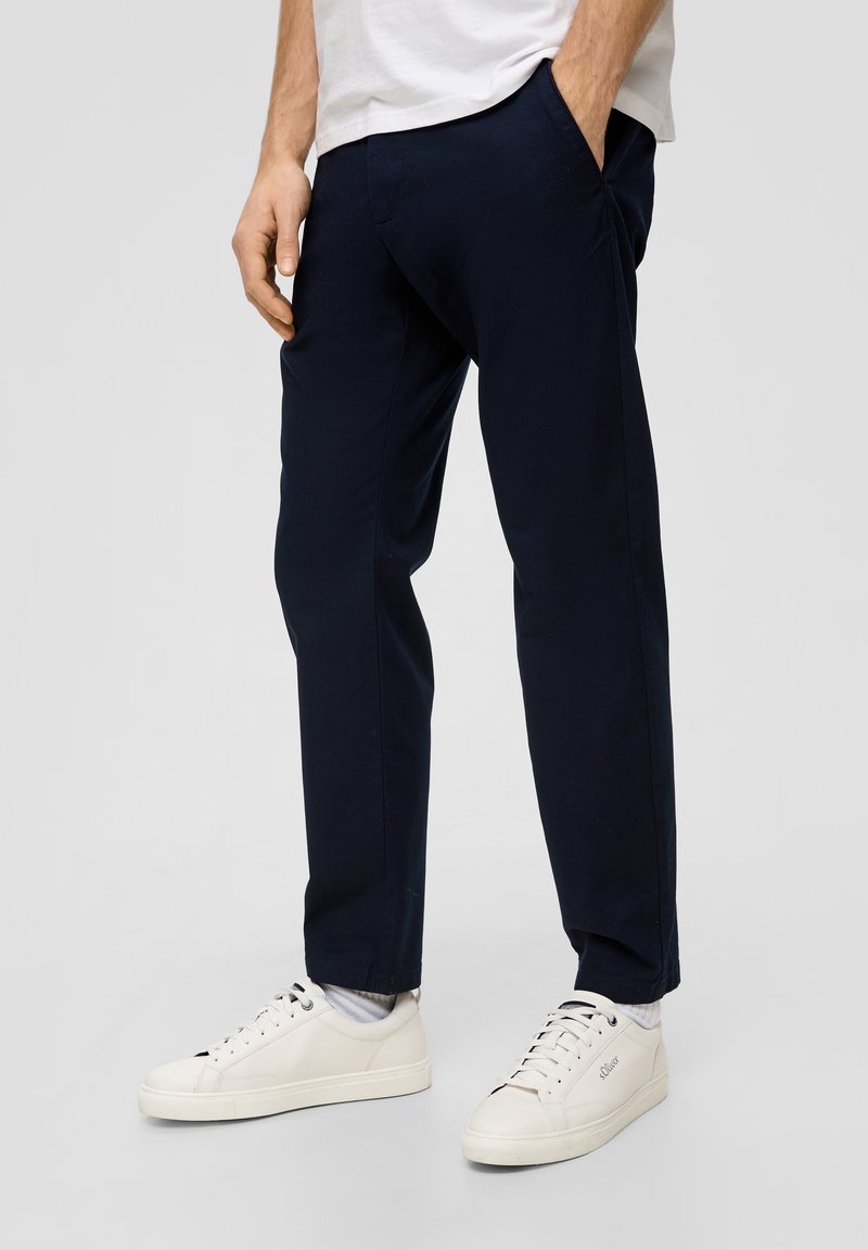 Granatowe spodnie zwężane z teksturowanej tkaniny, wyposażone w kieszenie boczne i połączone z białymi sneakersami, prezentujące elegancki design i czyste linie.