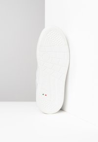 White sneaker sole with textured rubber, featuring a circular pattern and branding. Includes colored accents of green, white, and red.