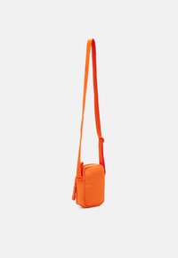 Orange crossover-veske med rektangulær form, justerbar stropp, glidelås og glatt tekstur. Kompakt design for enkel bæring.