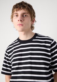 Tricou cu dungi negre și albe, cu decolteu rotund și mâneci scurte. Țesătură din bumbac texturat, cu un mic logo brodat pe piept.