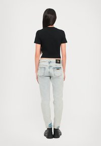 Juodas apkirptas marškinėliai su trumpomis rankovėmis, derinami su šviesiai mėlynomis džinsinėmis kelnėmis, kurios turi užtrauktuką ant užpakalinio kišenės ir juodą prekės ženklo etikėtę. Juodi batai.