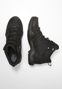 Czarne buty trekkingowe o wysokim kroju, z teksturowaną tkaniną na cholewce, solidną podeszwą z bieżnikiem oraz metalowymi akcentami na sznurowadłach.