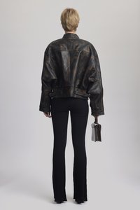 Veste en cuir noir avec une finition marbrée, coupe oversize, ourlet côtelé, associée à un pantalon à pattes d'eph côtelé noir et un petit sac élégant.