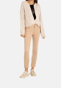 Cardigan côtelé beige clair avec des manches longues, une poche avant, associé à un pantalon beige clair ajusté et des baskets crème.