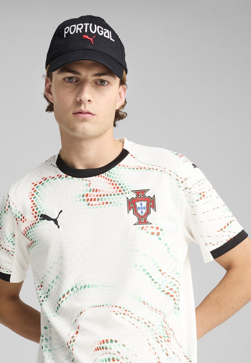 Biała koszulka sportowa z czerwonymi i zielonymi wzorami, z herbem piłkarskim Portugalii i logo PUMA. Czarna czapka z napisem "PORTUGAL".