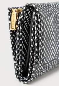 Αρκεη φακελος σε μαυρόασπρο σχεδιο με λευκά σχήματα σταγόνας, διπλωμένο σχέδιο και χρυσό φερμουάρ με χάραξη του ονόματος της μάρκας.