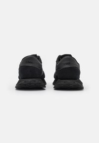 Schwarze Sportschuhe aus einer Kombination von glattem und strukturiertem Wildleder, mit flachem Absatz, mehrschichtiger Außensohle und minimaler Markenkennzeichnung auf der Rückseite.