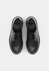 Black leather shoes with a smooth finish, rounded toe, lace-up design, and minimalistic branding on the insoles. Flat rubber soles.
