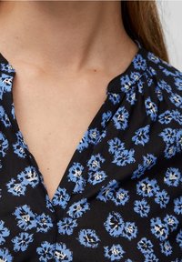 Maglietta nera con scollo a V, caratterizzata da un motivo floreale in blu e bianco. Il tessuto sembra leggero con una sottile texture.