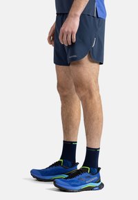 Navy atletiska shorts med reflexdetaljer, parat med blå och svarta löparskor med gröna accenter. Texturerade strumpor fulländar looken.
