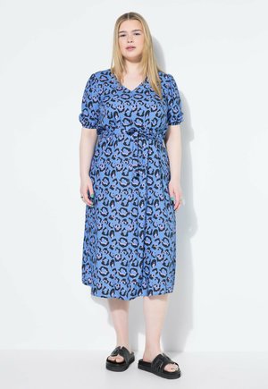 Vestido de estampado de leopardo azul con escote en V, mangas cortas enrolladas y cintura ceñida con cinturón. Hecho de una tela liviana, cae hasta la mitad de la pantorrilla. Sandalias negras.
