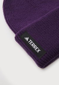 Beanie viola in maglia realizzato in stoffa testurizzata, con un'etichetta nera con la scritta "TERREX" in lettere bianche.