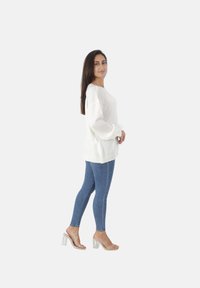 Witte gebreide trui met een ontspannen pasvorm en ribbelrand, gecombineerd met blauwe skinny jeans en heldere hakken. Eenvoudig ontwerp, zachte textuur.